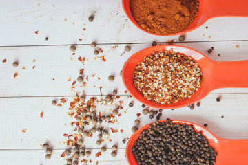 Spices in orange spoon on white wooden background. seasoning delicious food. Paprika, black pepper peas, Gross natural sea salt mixed with dried red hot chili pepper, colorful seasoning close-up