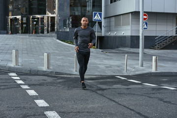 Urban workout. Full length portrait of athletic african man in sportswear running on the road in early morning. Sport motivation concept.