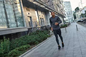 Morning workout. Young and strong african man in stylish sportswear running in the city