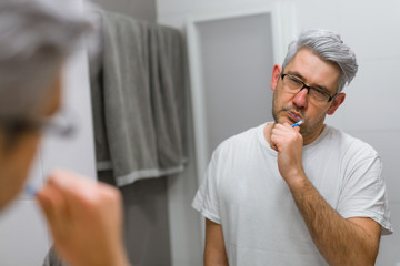 sleepy middle aged man brushing teeth in bathroom