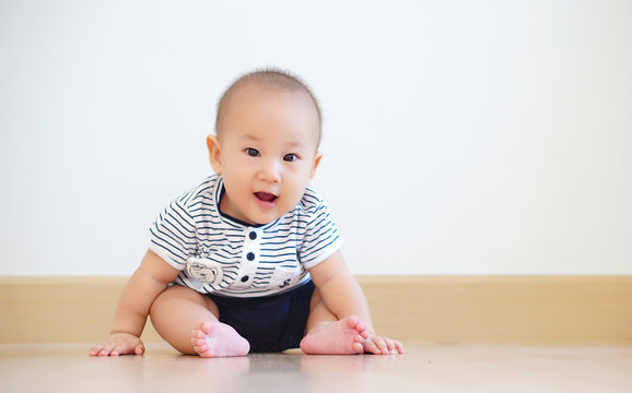 Cute baby boy smiling and sitting on wooden floor in white blank room