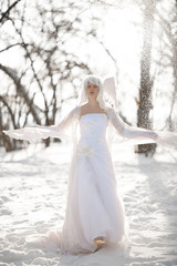 Fototapeta na wymiar Beautiful girl stands in snowy forest in image of good angel against background of snowfall.