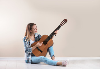 Young woman playing acoustic guitar near grey wall. Space for text