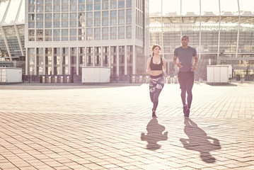 Obraz premium Positive and sporty mixed race couple: handsome african man and brunette girl in sportswear running together on a sunny warm day.