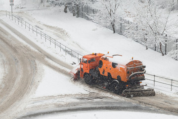Orange snow plow truck or street sweeper machine cleans the road surface from snow. February snowfall