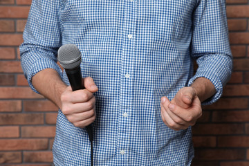 Man in shirt holding microphone near brick wall, closeup