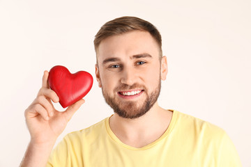 Young man holding wooden heart on white background