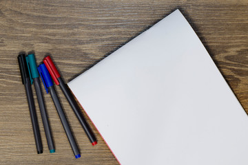 Blue, red, green and black markers and a white sheet of paper on the table.
