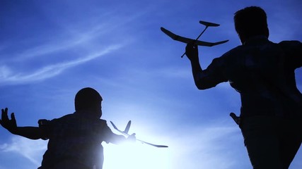Silhouette of two boys running with airplanes at sunset