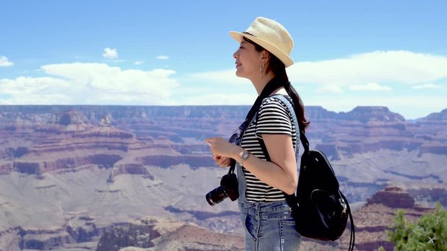 cheerful female asian backpacker with camera using smartphone taking picture of nature view from mountain in Grand Canyon National Park. travel tourism photography concept. happy woman sightseeing
