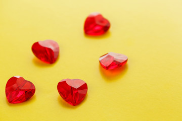 Heart shaped red crystals pattern on yellow background. Jelly crisscallic hearts on top. View from above.
