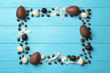 Frame made of chocolate Easter eggs on color wooden background, top view with space for text