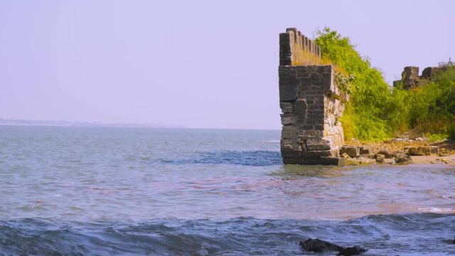 Moss and tree covered stone wall ending in ocean waves from diu fort in gujarat india