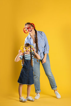 Happy woman and daughter with funny glasses on color background