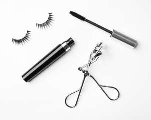 Curler, mascara and false eyelashes on white background, flat lay