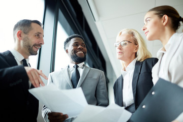 Four confident traders with financial documents interacting about situation on stock brokerage at...