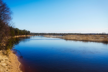 photograph of a rural-style autumn landscape with a river and a beach in the foreground, and a curved bridge in the background