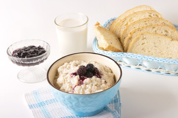 Healthy breakfast with a glass of milk, homemade oatmeal with blackberries in a blue bowl and fresh cereal bread on a light background