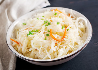 Fermented cabbage. Vegan food. Sauerkraut with carrot and spices in bowl on the dark background. Trend food.