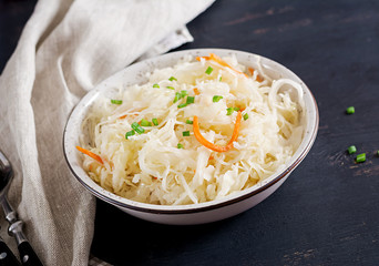 Fermented cabbage. Vegan food. Sauerkraut with carrot and spices in bowl on the dark background. Trend food.