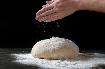 Obraz premium Female hands sprinkling flour over fresh dough on dark background.