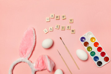 Happy Easter concept. Preparation for holiday. Inscription HAPPY EASTER letters eggs colorful paints and bunny ears isolated on trendy pink background. Simple minimalism flat lay top view copy space
