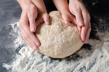 Mother and child hands prepares the dough with flour on dark wooden table. Bakery background.
