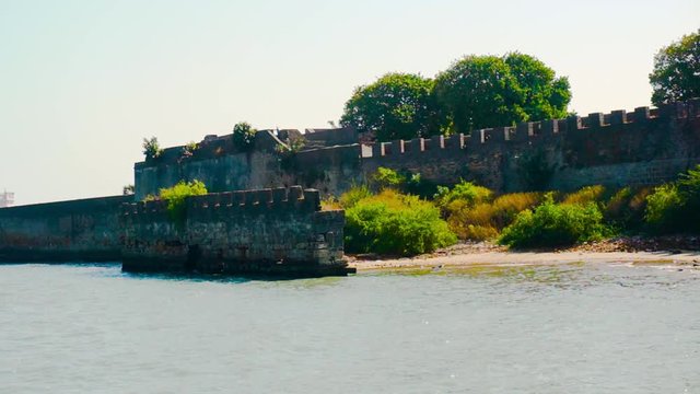 Moss and tree covered stone wall ending in ocean waves from diu fort in gujarat india