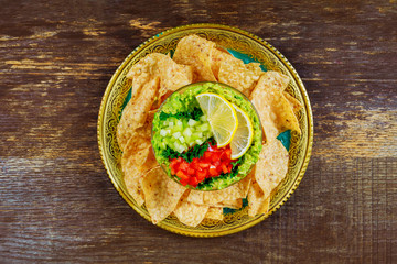 Green guacamole with nachos and avocado on wood background