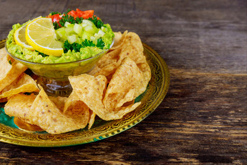 Guacamole with tortilla chips in a bowl on a dark wood background. Top view with copy space.