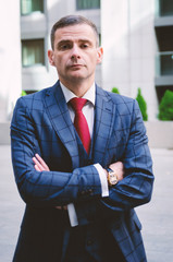 Serious business man in a fashionable stylish checkered suit on the background of a concrete gray business center (offices). Business life in the city.