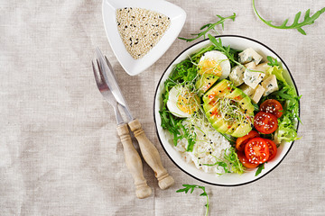 Healthy green vegetarian buddha bowl lunch with eggs, rice, tomato, avocado and blue cheese on table. Trend cuisine. Top view. Flat lay