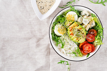 Healthy green vegetarian buddha bowl lunch with eggs, rice, tomato, avocado and blue cheese on table. Trend cuisine. Top view. Flat lay