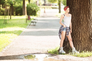 Young beautiful woman with inline skates lleaning on a tree in park