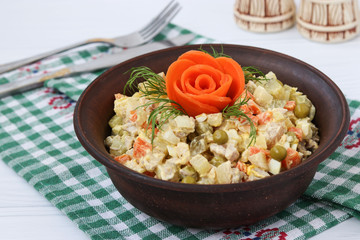 Salad "Olivier" of pickled cucumbers, meat, carrots, pickled peas, boiled eggs and potatoes in bowl on a white background. Salad is decorated with a rose of carrots