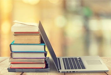 Stack of books with laptop on wooden table