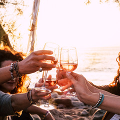 people drinking at party. group of friends white wine in hand toasting with glasses. close up on hands and drinks - beautiful scenic sunset and ocean in background for outdoor leisure activity 