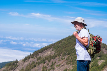 Fototapeta na wymiar Lonely adult aged trekker with backpack standing and looking at the beautiful landscape at the mountains - trekking and hiking for mature people in outdoor leisure activity - travel and blue sky