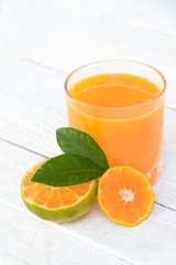 a glass of orange juice and fresh oranges on white wooden base
