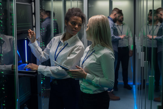 Two women are working in a data center with rows of server racks