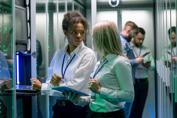 Two women are working in a data center with rows of server racks