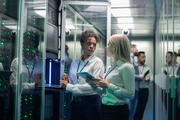 Two women are working in a data center with rows of server racks - obrazy, fototapety, plakaty
