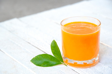 a glass of orange juice on white wooden base