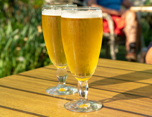Two cold light unfiltered beer in glasses served on sunny outdoor terrace in garden