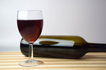 glass of wine and bottle of red wine on wooden table