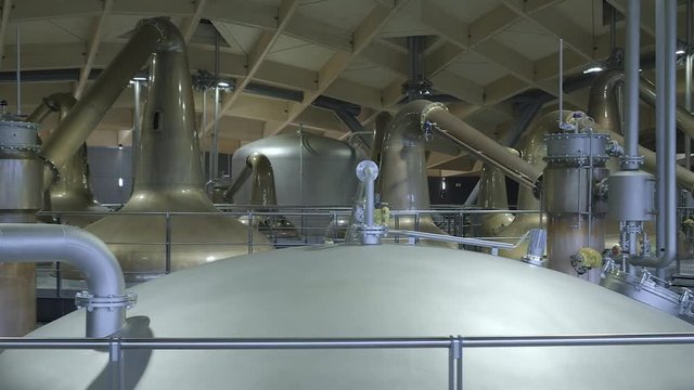 Interior pipework, copper stills and mash tuns highlighting the architecture and complexity of a modern Scottish whisky distillery. Pan left to right.