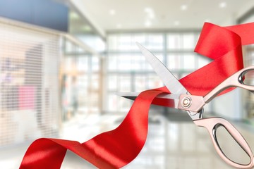 Scissors cutting red ribbon, close-up view on blue background