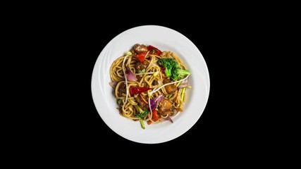 Rotating udon stir fry noodles with meat or chicken and vegetables isolated on ablack background. Top view