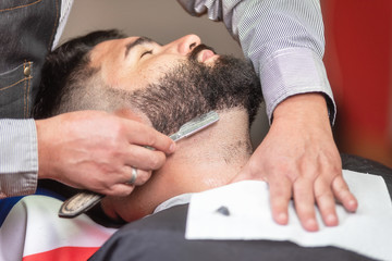 Handsome man having a shave with vintage razor at the barbershop .