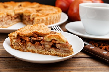 Closeup piece of homemade apple pie with cinnamon and cup of tea on wooden table. Shallow focus.